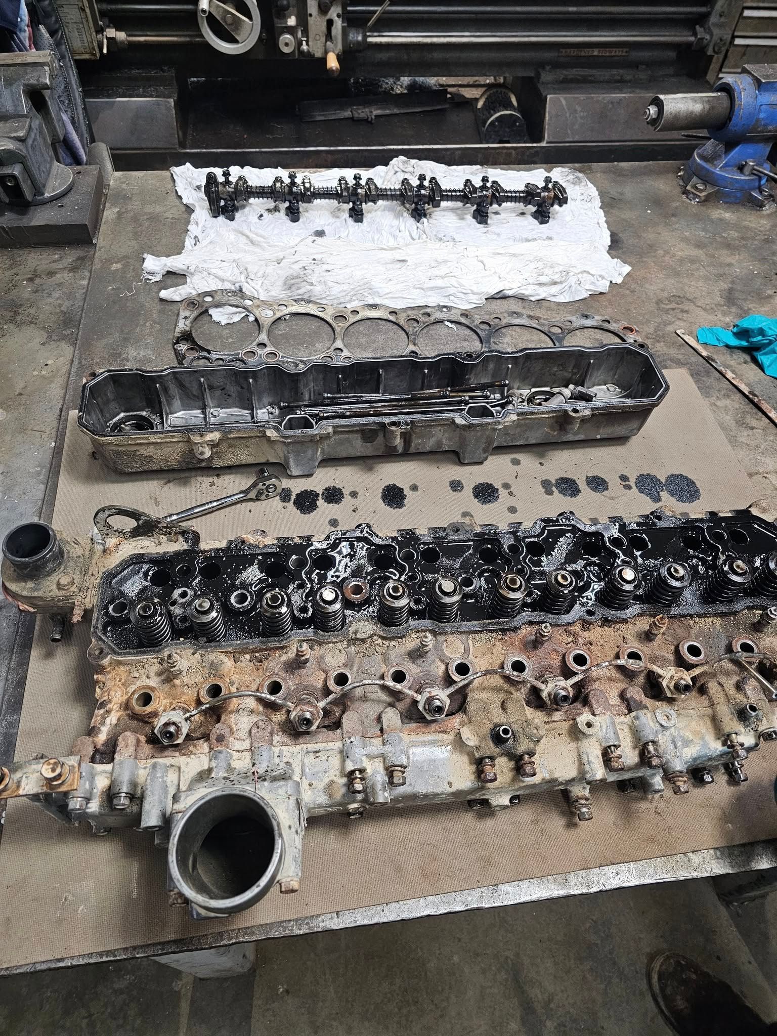 Three disassembled, oil-covered engine parts laid out on cardboard in a workshop.