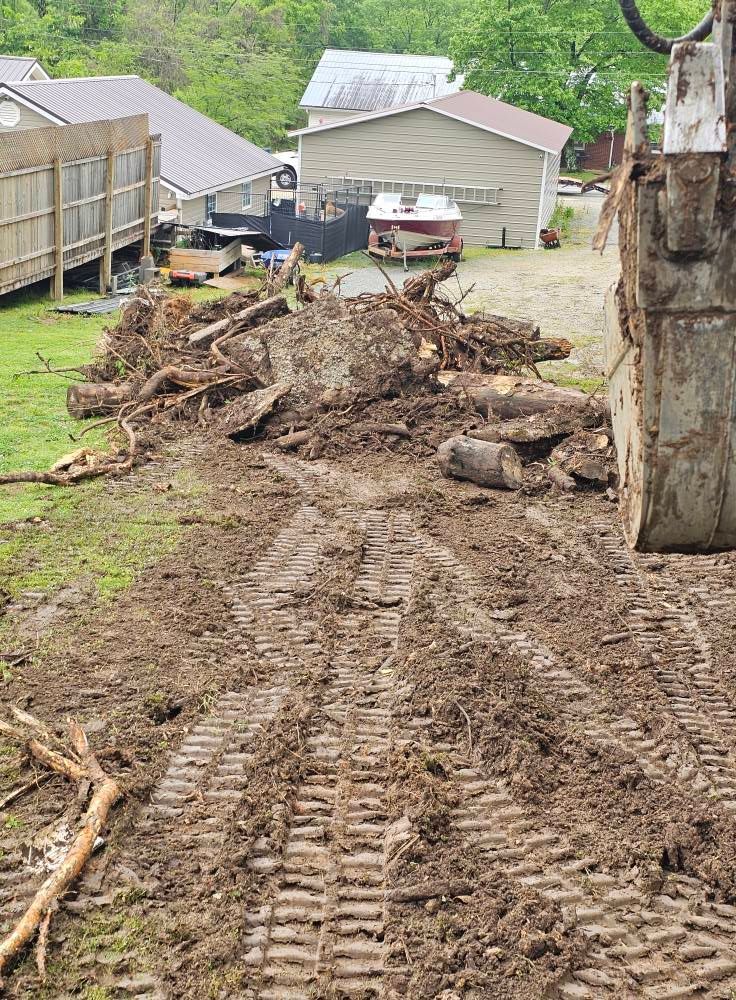 Dirt driveway blocked by mud and logs after a landslide, with houses and a large tree nearby