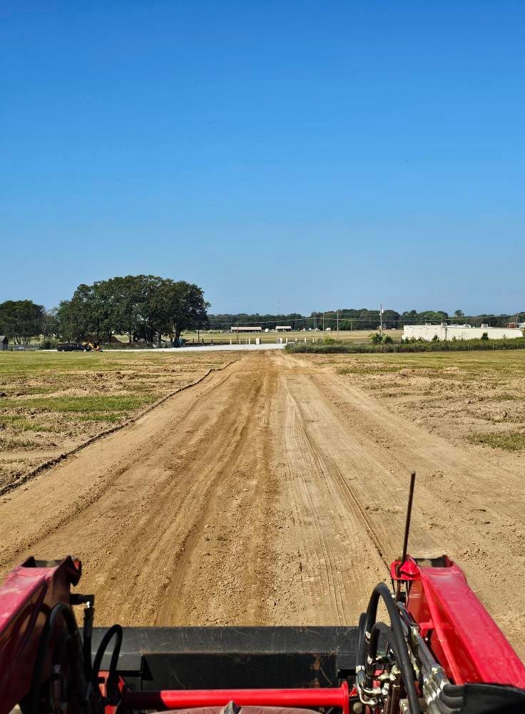 View from a red tractor driving down a dirt road through open fields under a clear blue sky