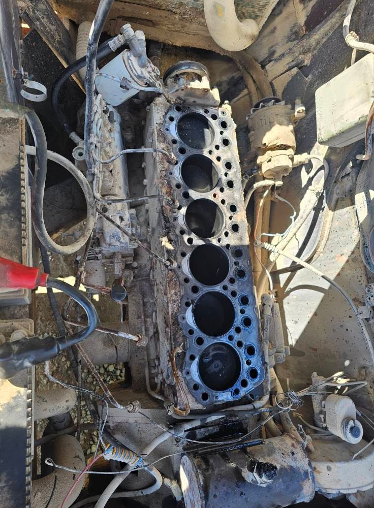 Engine block in a dirty vehicle bay, with exposed cylinders and scattered hoses and wires