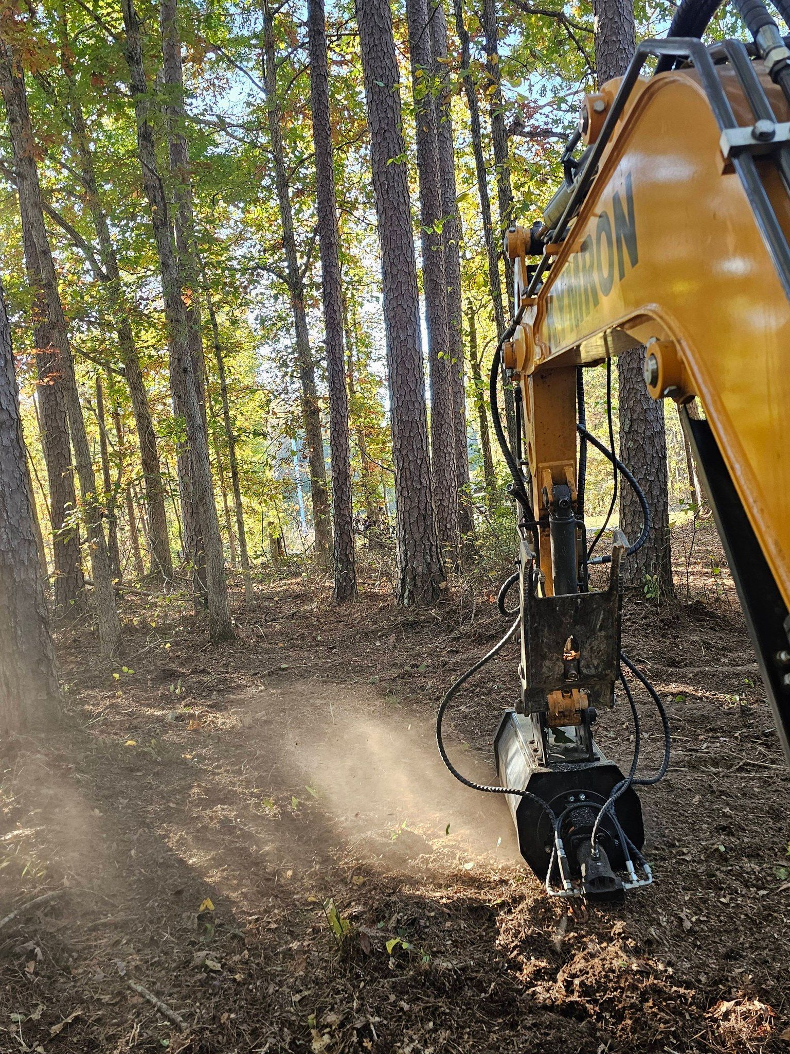 Cleared dirt lot with trees along the edge and a yellow construction vehicle at right