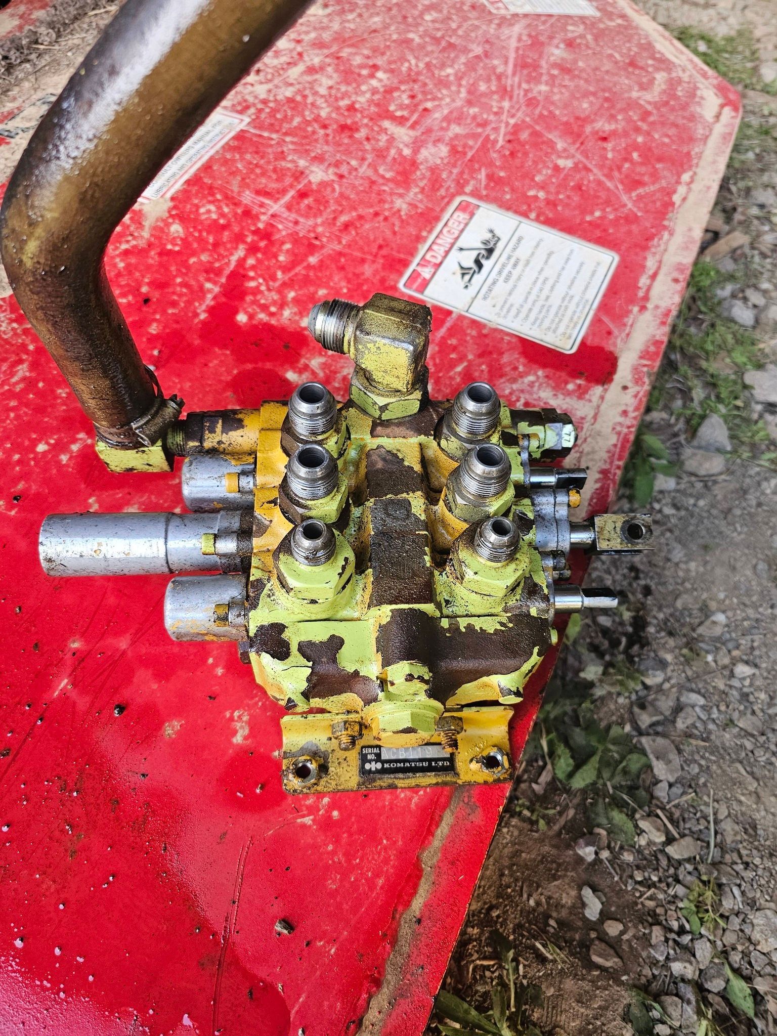 Hydraulic valve block with hoses on a red workbench outdoors, coated in grease and dirt