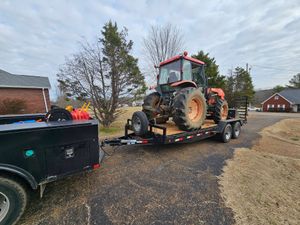 Tractor loaded on a flatbed trailer behind a black truck on a rural driveway