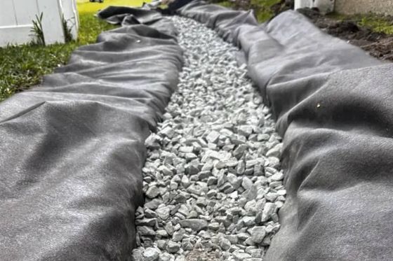 Gray landscape fabric lining a gravel drainage trench beside a white building