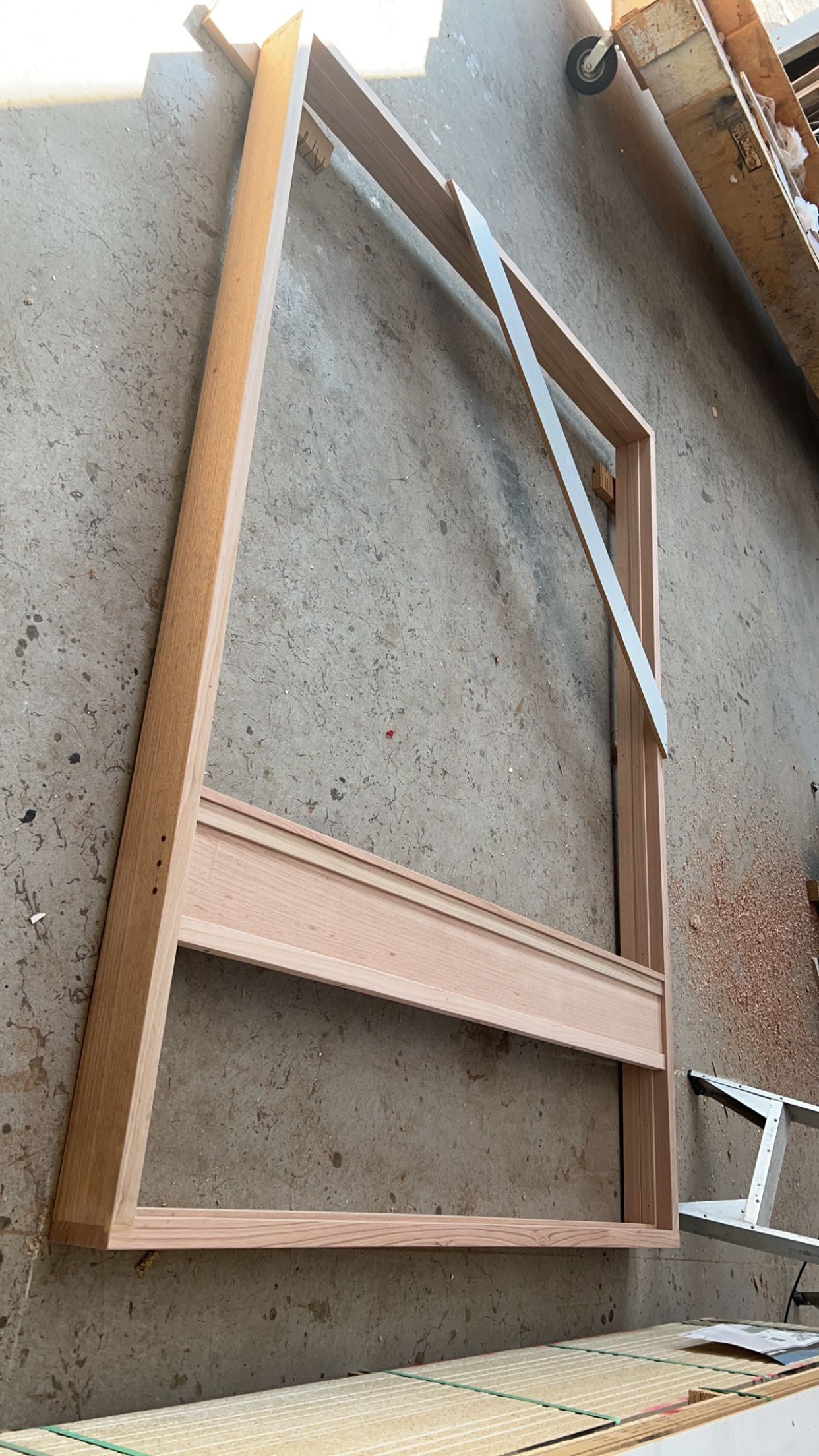 Wooden frame construction, partly assembled, resting on a concrete surface.