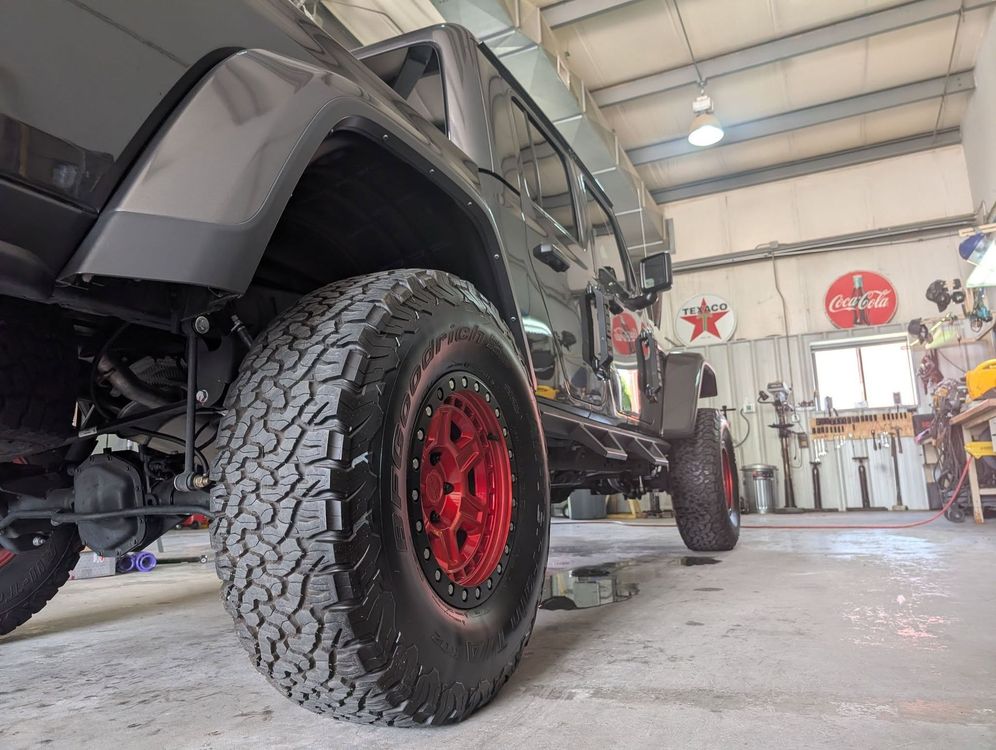 Black off-road Jeep with red rims in a garage workshop, low-angle view