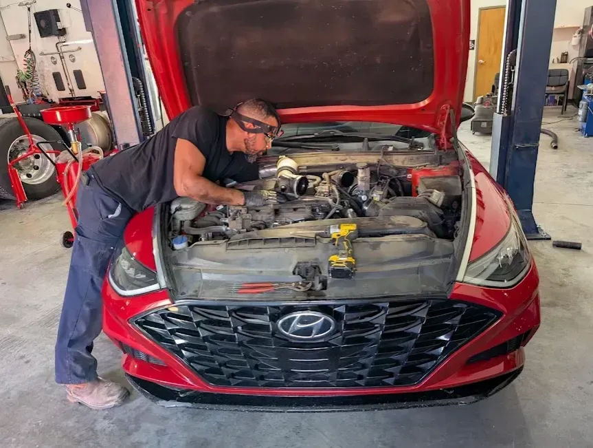 Mechanic leaning into a red Hyundai’s open hood in an auto shop