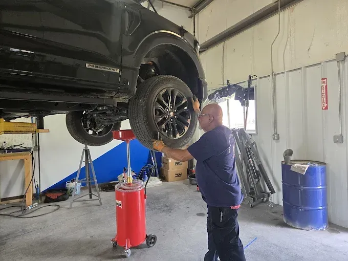 Mechanic working under a black SUV lifted in an auto repair shop, using a red jack stand