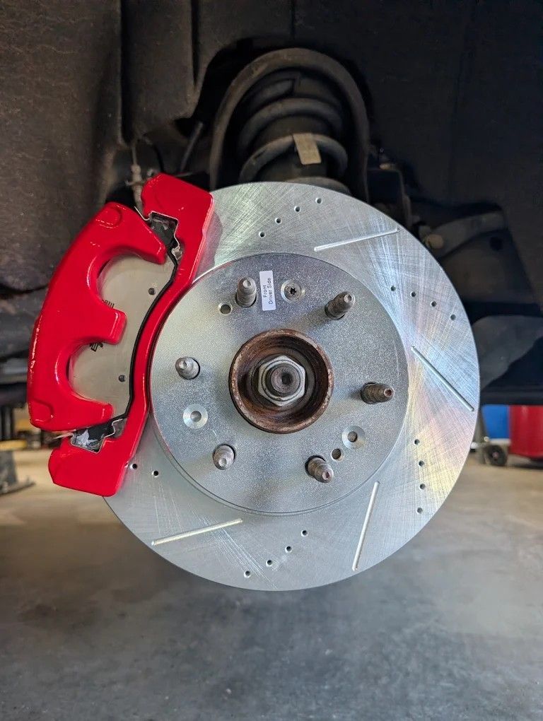 Close-up of a car brake rotor with a bright red brake caliper inside a wheel well