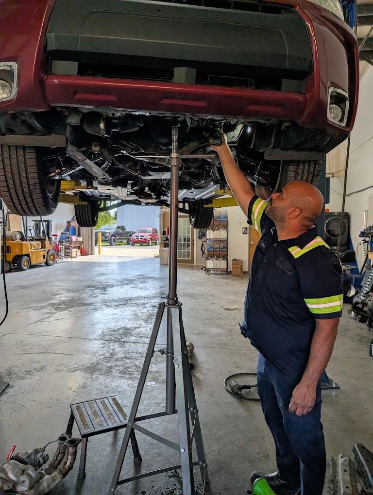 Mechanic inspecting the underside of a red car on a lift in an auto repair shop