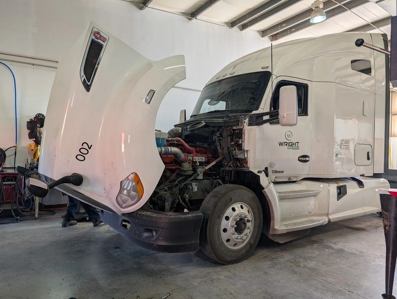 White semi-truck in a garage with its hood open, exposing the engine.