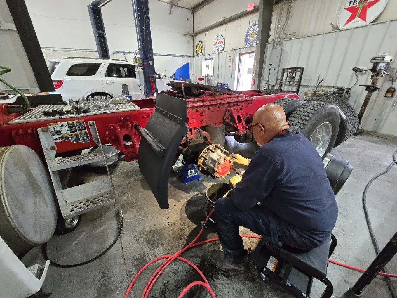 Mechanic in a shop working on a red vehicle chassis with tools and cables nearby