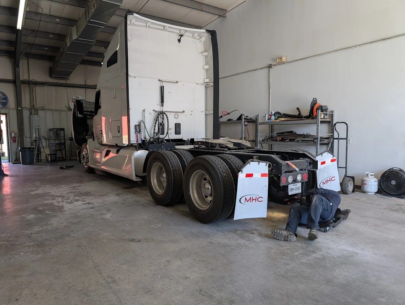 Truck chassis in a garage bay, with rear wheels and tools beside a workbench.