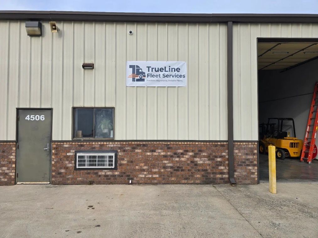 Industrial building exterior with TrueLine sign, brick base, gray door, and yellow bollard by open bay.