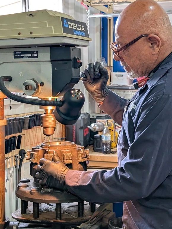 Man inspecting a metal component under a drill press in a workshop