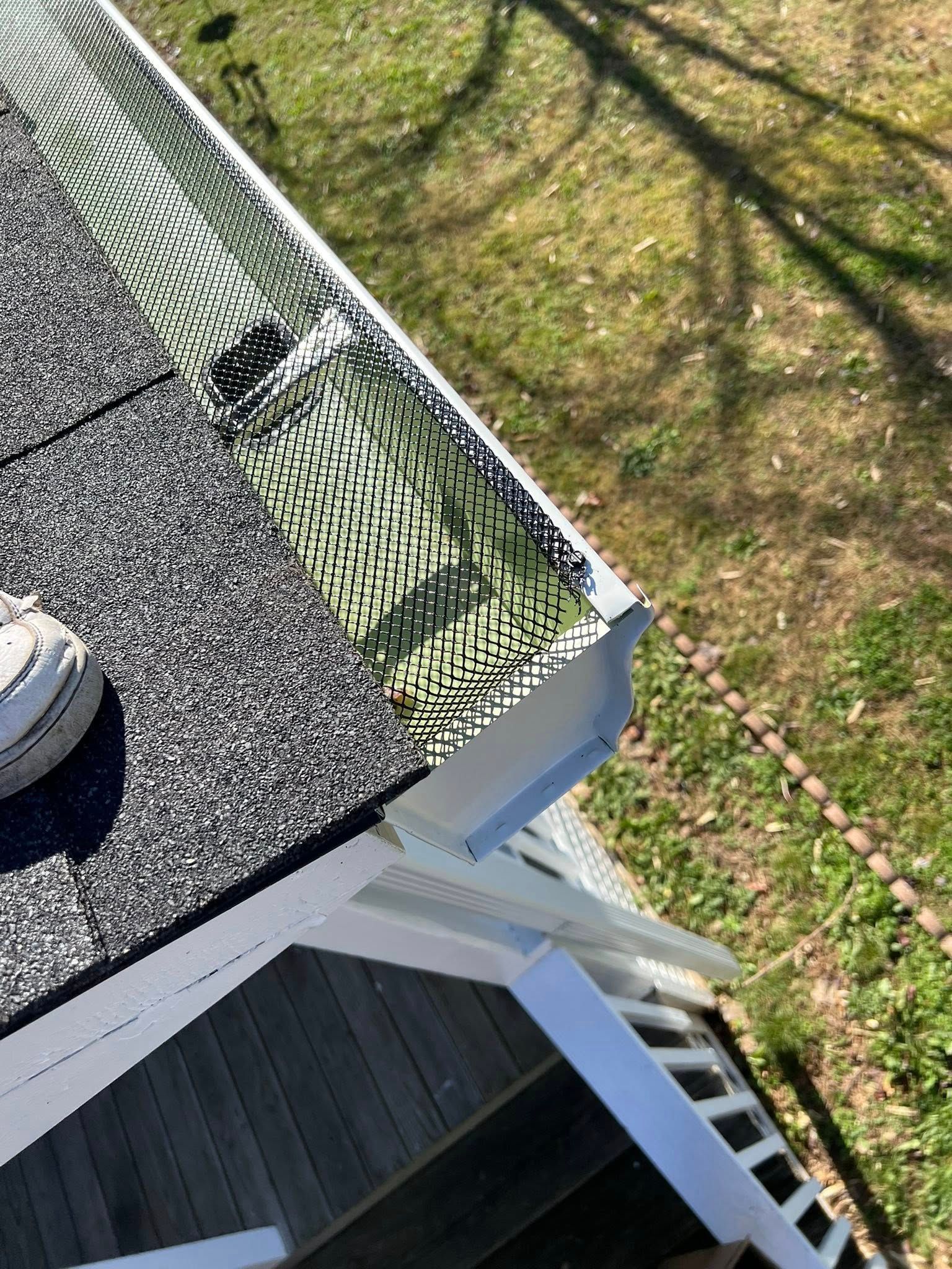 A high-angle view of a roof edge featuring a green mesh gutter guard installed over a white gutter above a wooden deck.