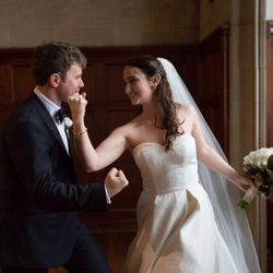 Bride and groom smiling in a wood-paneled room, holding hands during their wedding dance.