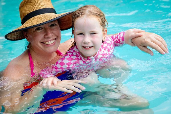 Woman and child smiling in a swimming pool, wearing sun hats and pink swimwear
