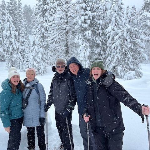 Four people in winter coats smiling in a snowy forest with ski poles and falling snow