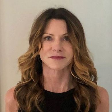 Portrait of a woman with long wavy brown hair wearing a black top against a plain light background