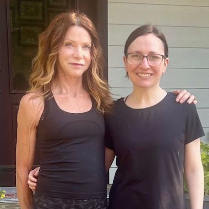 Two women standing together outdoors, smiling, in black tops.