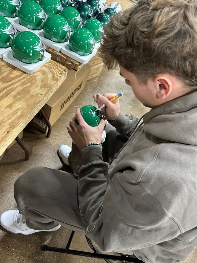 Man signing a green helmet, with other helmets in the background.
