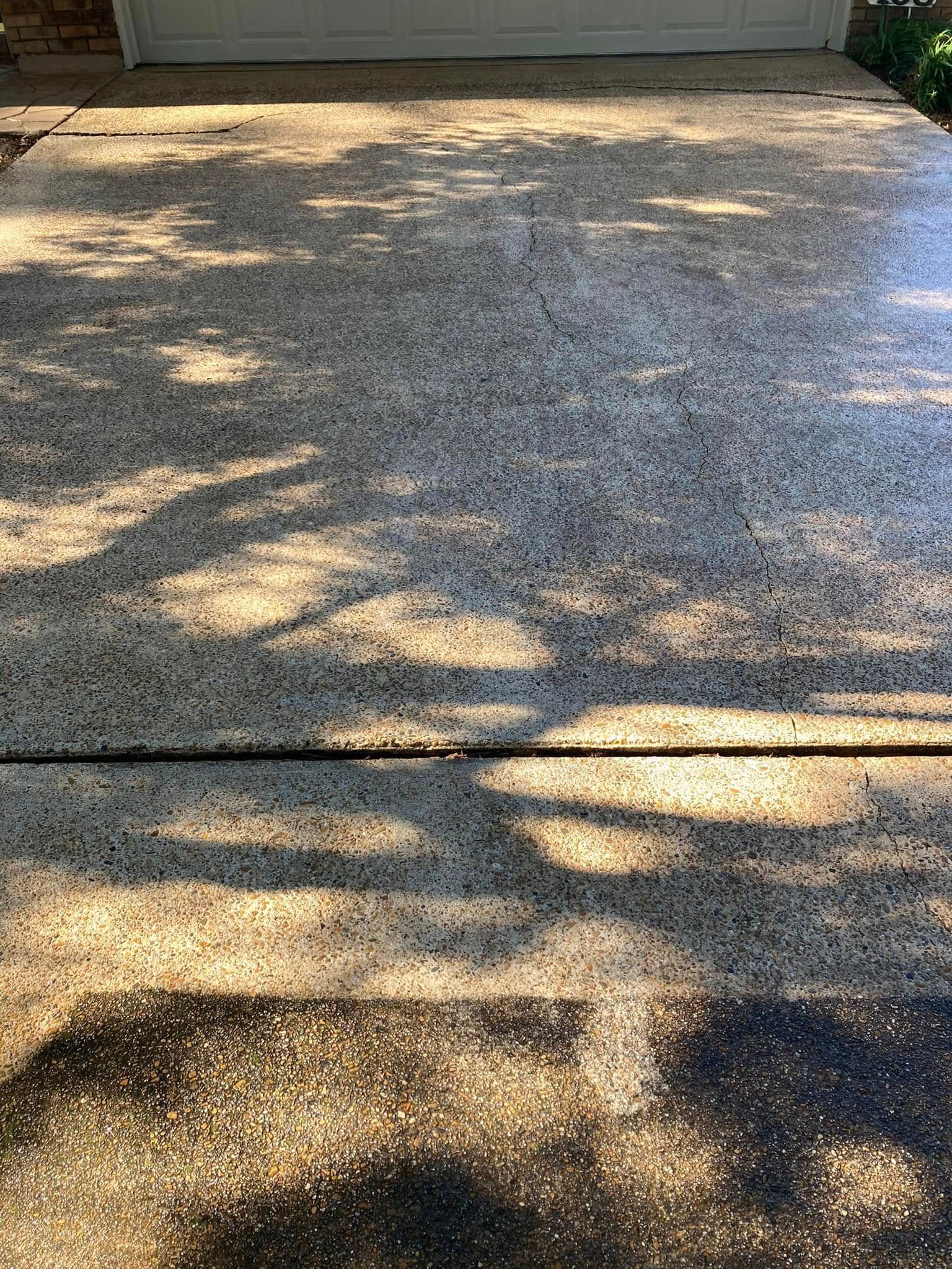 A textured concrete driveway surface with dappled light and tree shadows casting dark patterns across it.