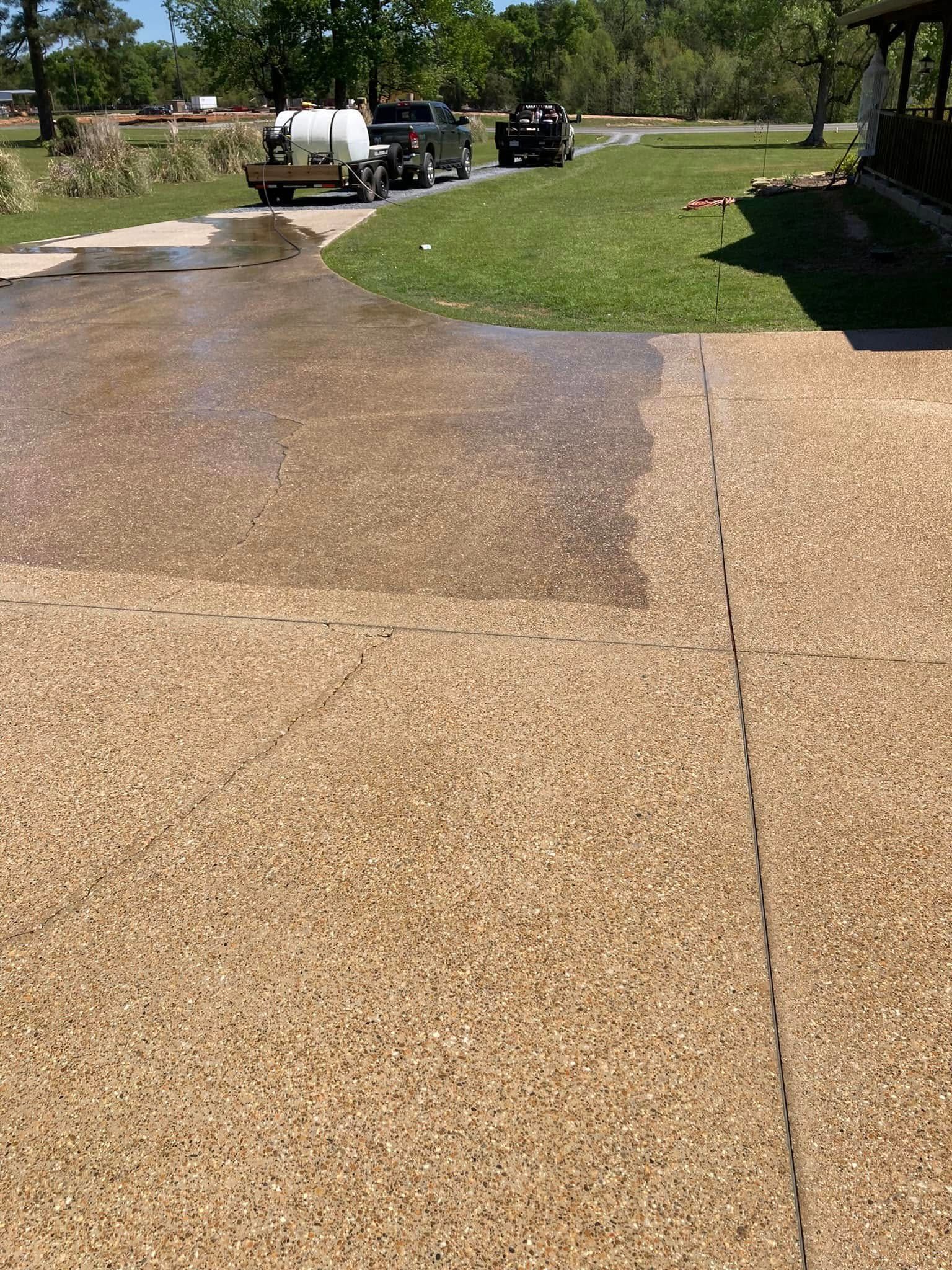 A power washer cleans a section of a textured gravel driveway, leaving a clear line between wet and dry areas.