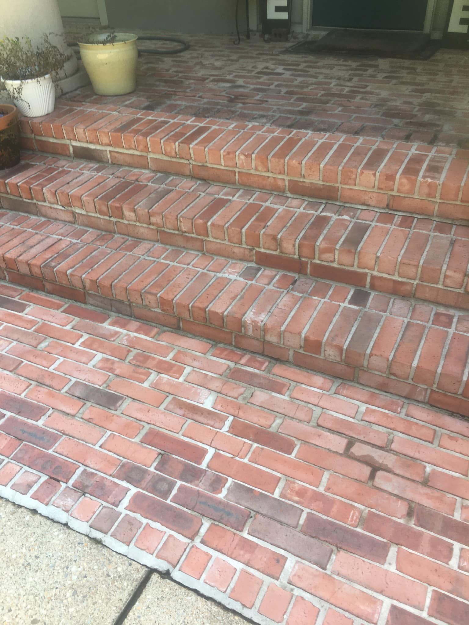 Three brick steps lead up to a porch with a reddish-brown brick walkway in the foreground.