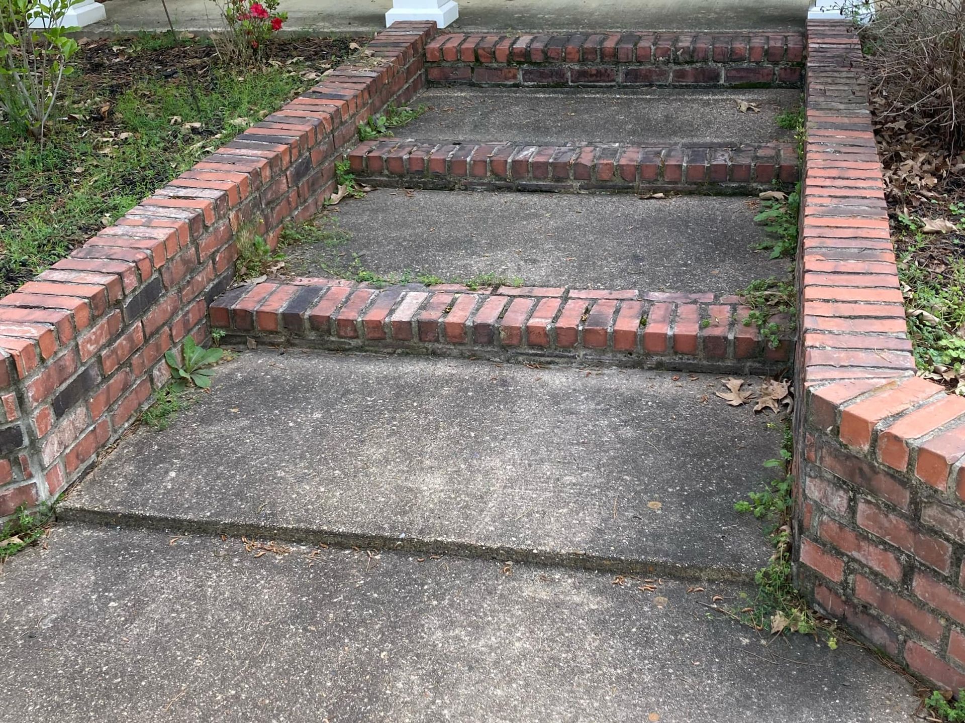 Three concrete steps with brick risers and brick side walls leading up to a building entrance.