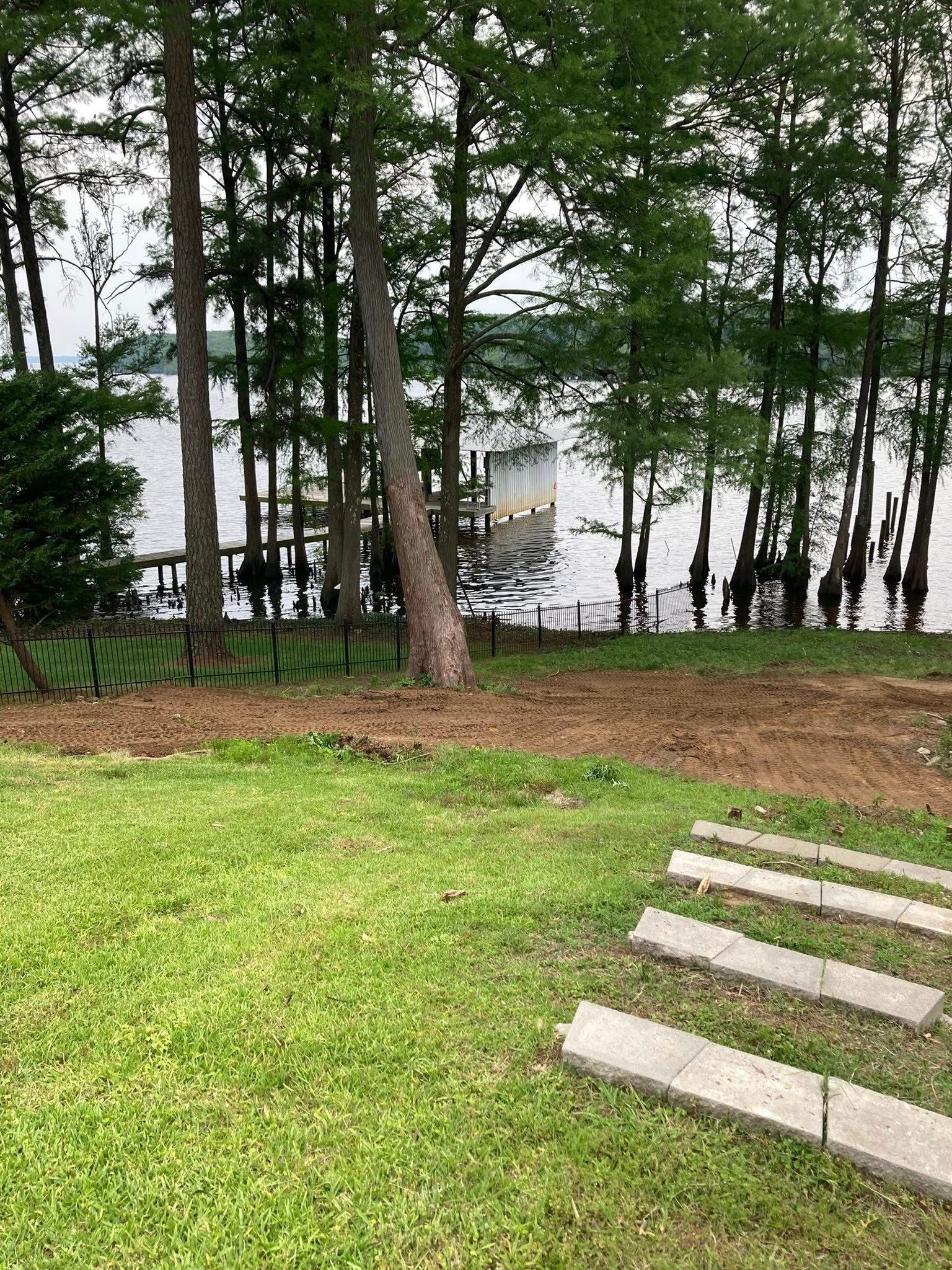 A backyard with a grassy slope leading toward a lake, featuring stone steps and a wooden pier in the distance.