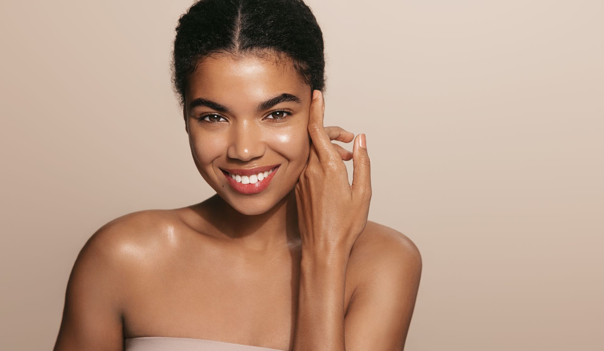 A woman is smiling and touching her face with her hand.