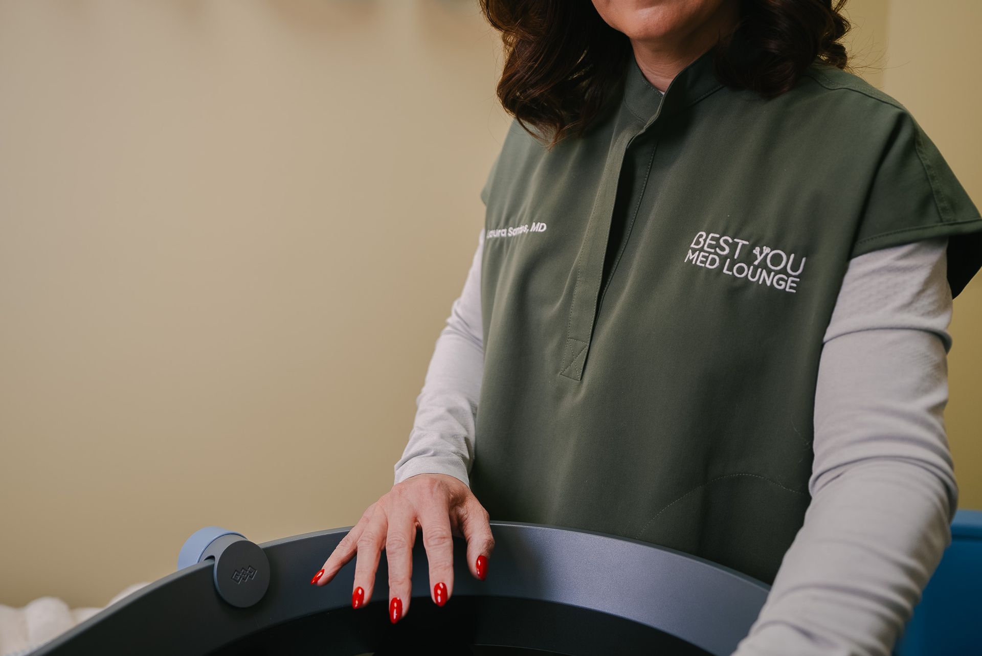 Person in green vest with red nails resting hand on a black treadmill console