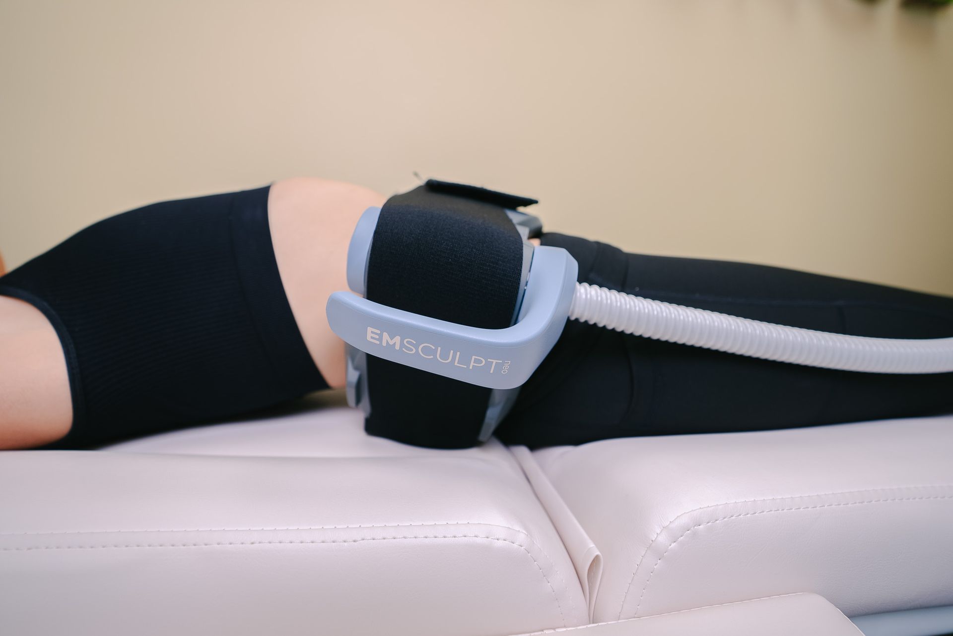Person lying on a white massage table with a black leg compression device strapped to the thigh.