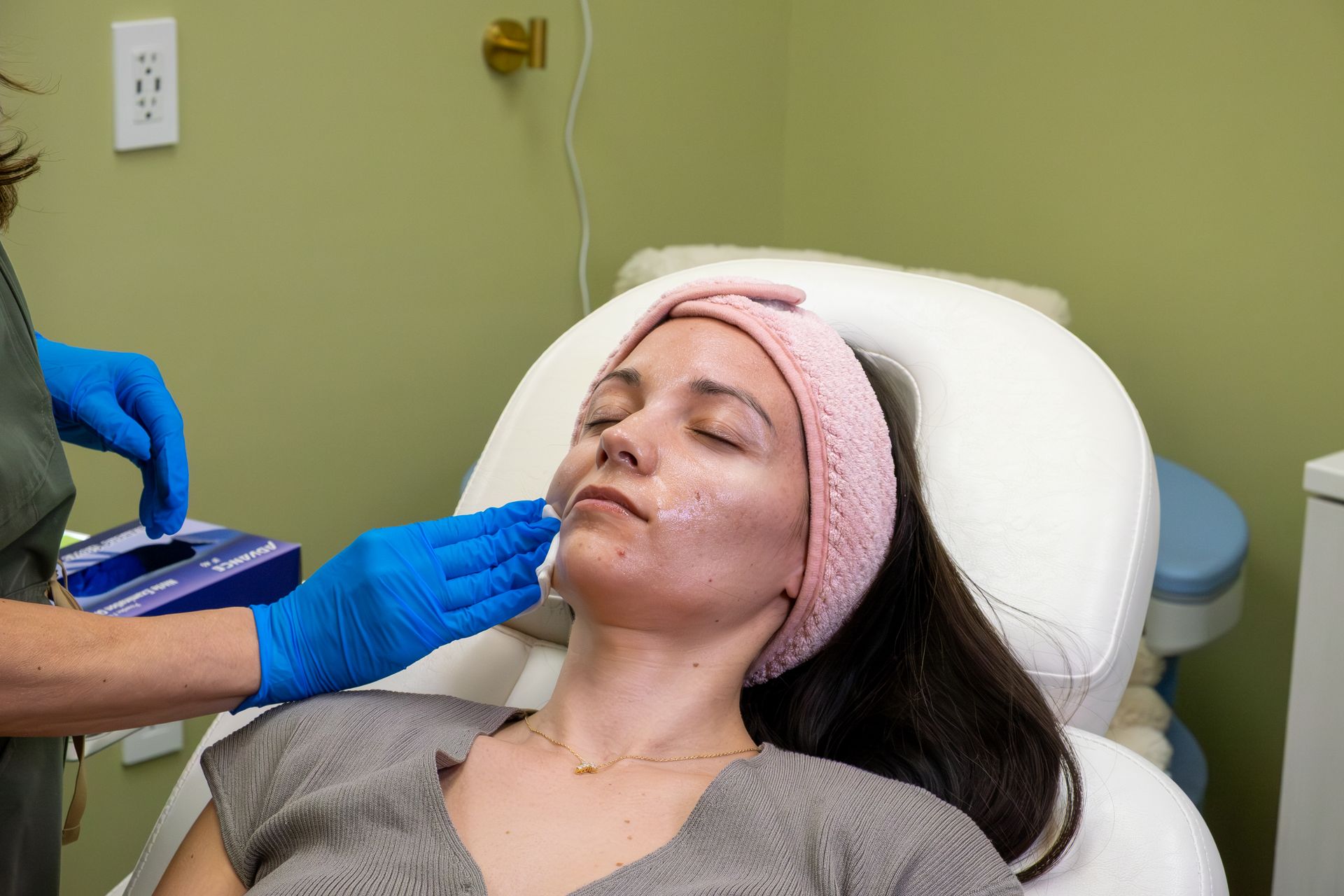 Cosmetic treatment being applied to a woman's face as she reclines in a clinic chair