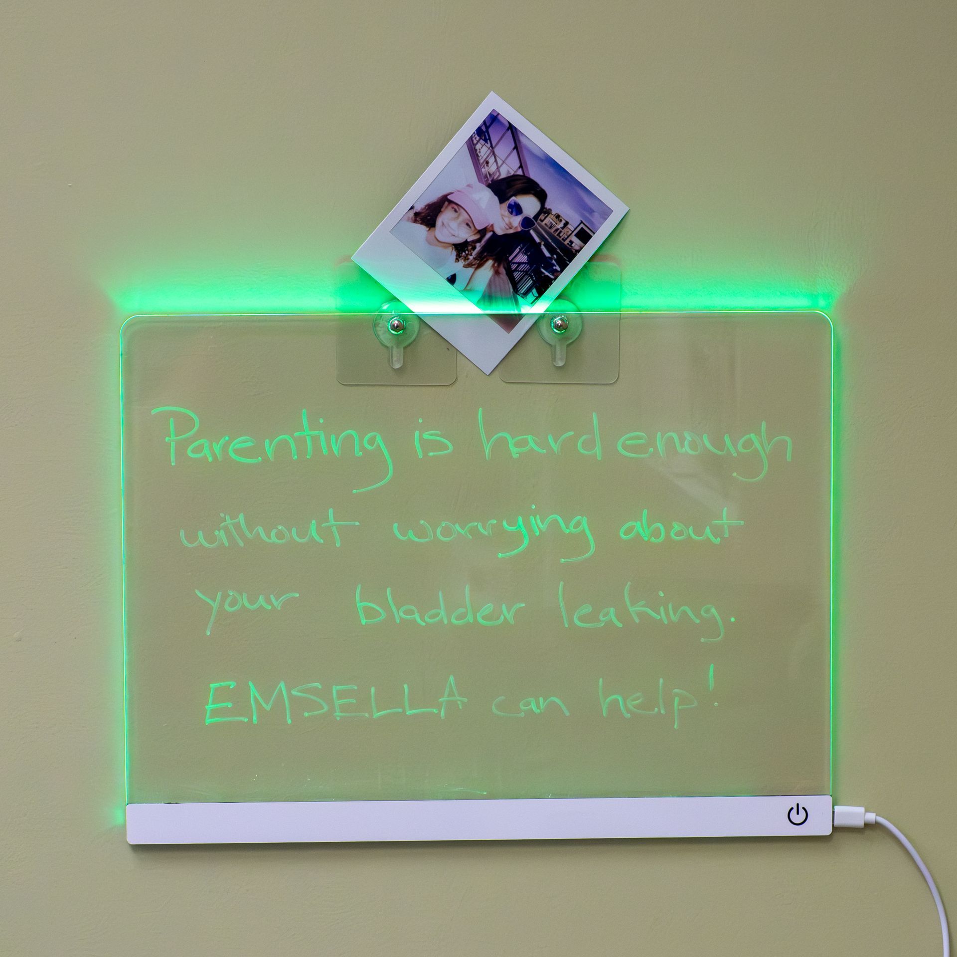 Green-lit whiteboard with handwritten quote, a small photo clipped on top, and a power cord at the bottom right
