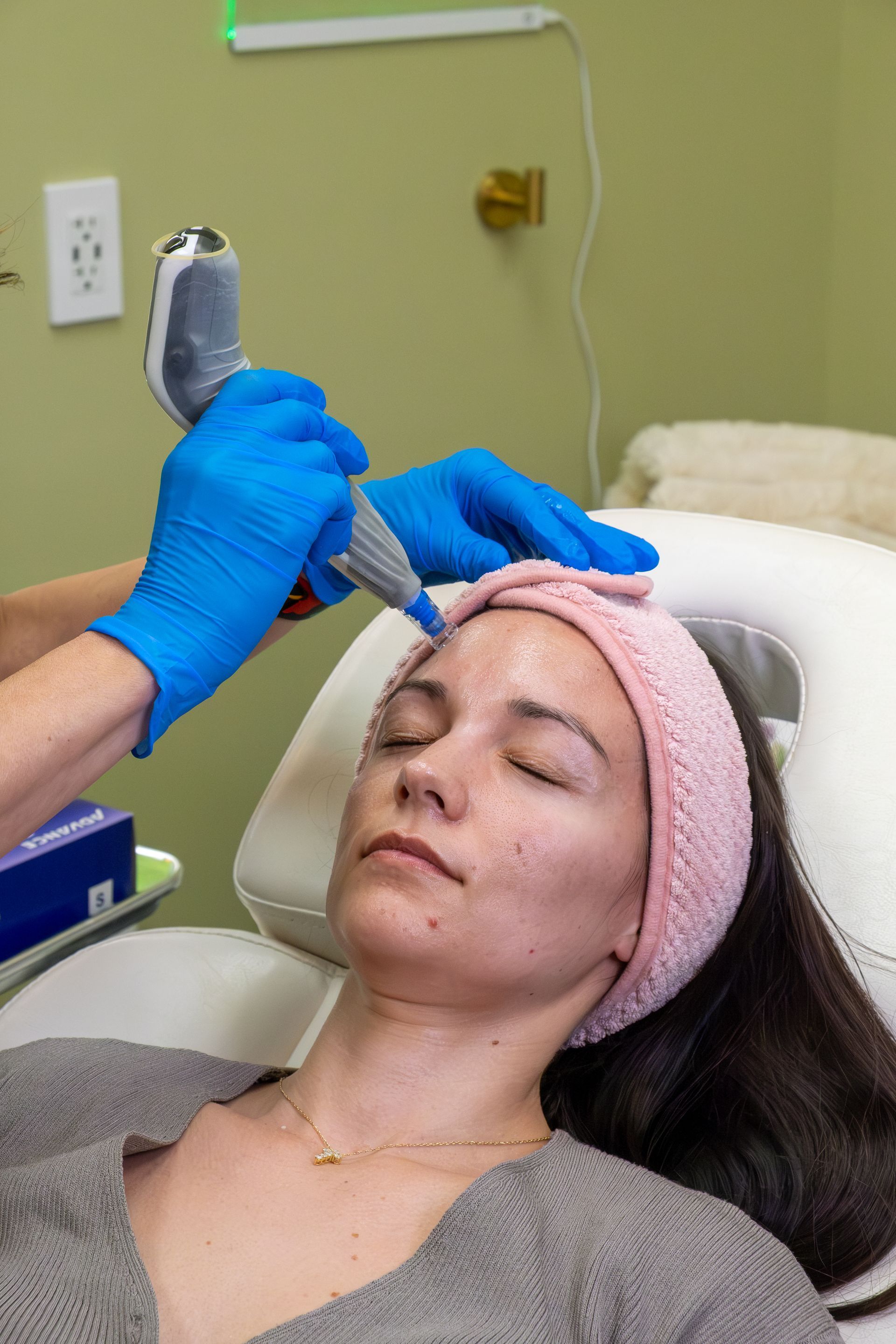 Esthetician using a handheld device on a reclined client’s face during a skincare treatment