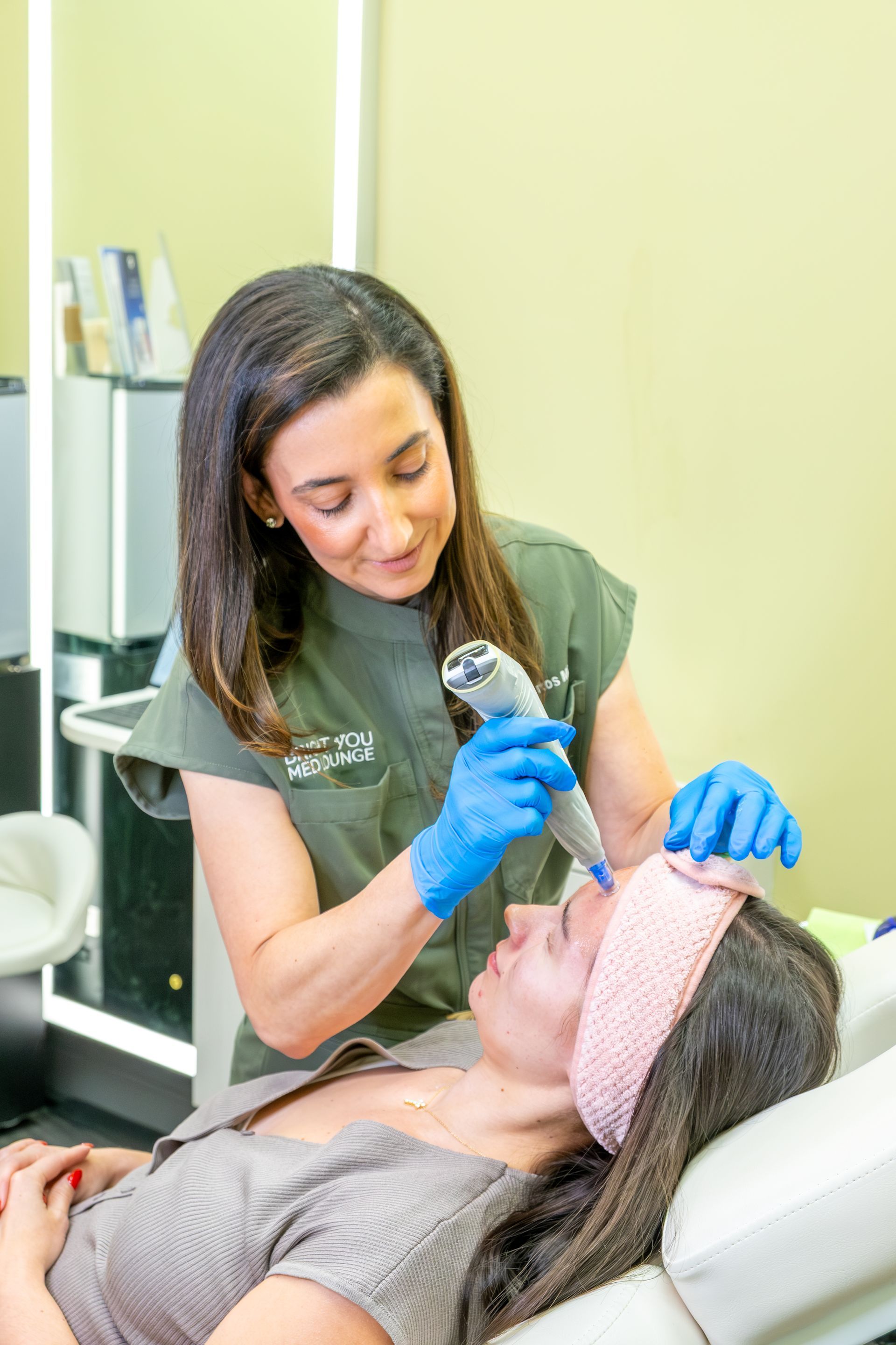 A dental hygienist in blue gloves examines a patient's mouth while the patient reclines in a dental chair.