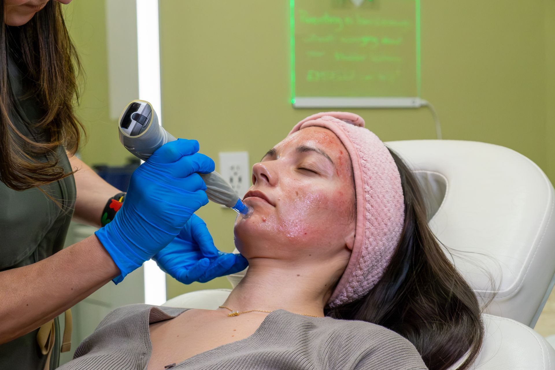 Cosmetic treatment in progress as a clinician uses a handheld device on a reclining patient’s face