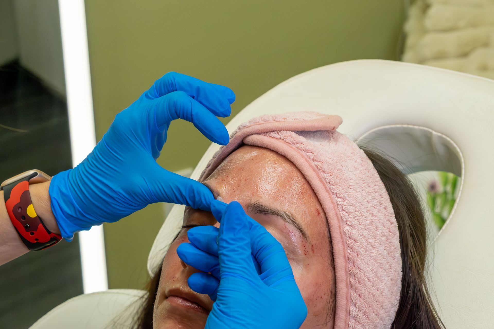 Gloved hands applying eyebrow treatment to a client lying back on a salon chair