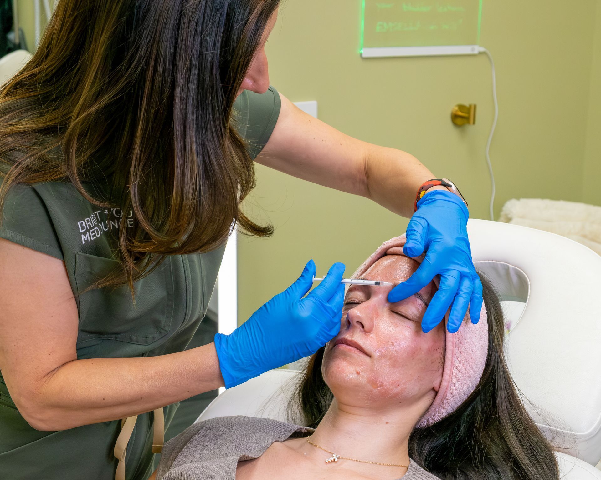 Esthetician wearing blue gloves performs a facial treatment on a reclined client in a treatment room