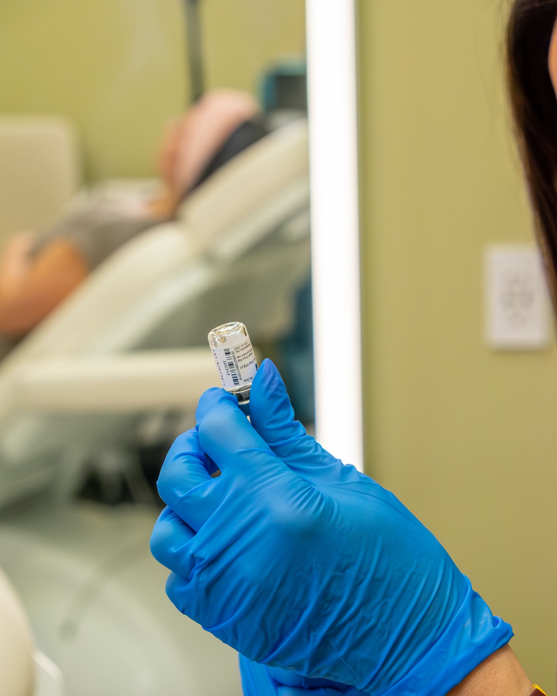 Blue-gloved hand holding a small dental impression tool in a clinic setting