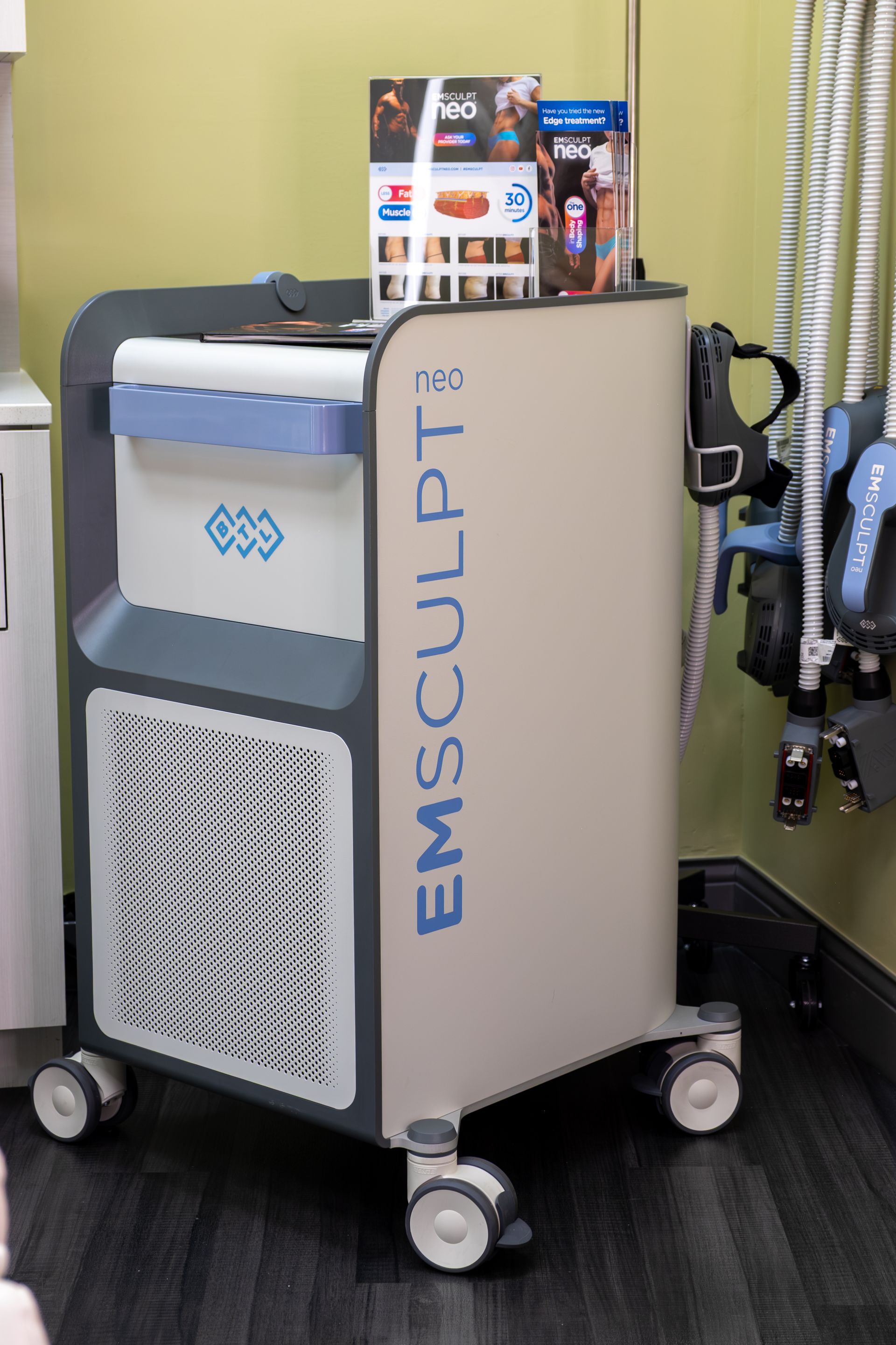 EMSculpt device on wheels in a clinic room, with brochures and exercise equipment nearby