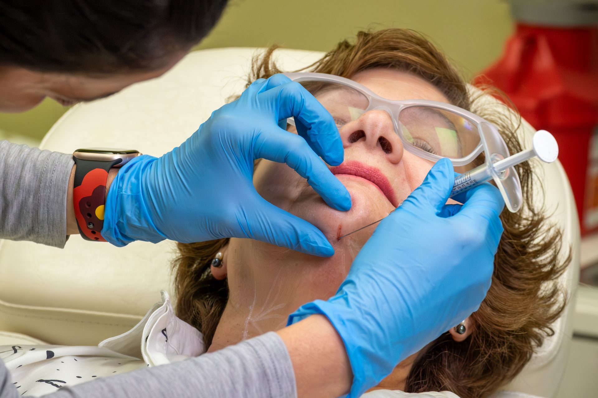 Dentist adjusting a patient’s mouth with blue gloves while the patient wears safety glasses.