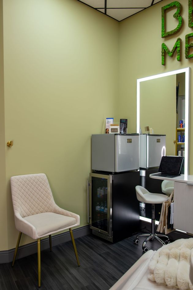 Small salon waiting area with a pink chair, black mini-fridge, and mirrored styling station.