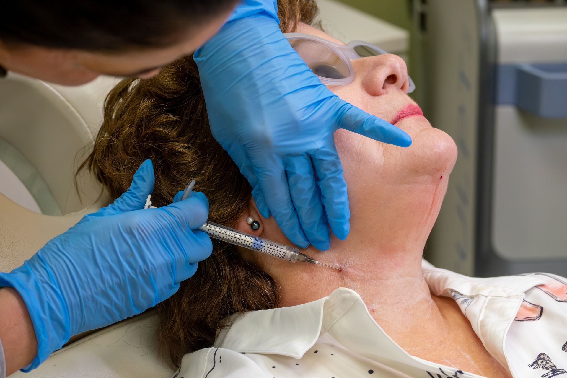 Gloved clinician administering a neck injection to a reclining patient in a medical setting