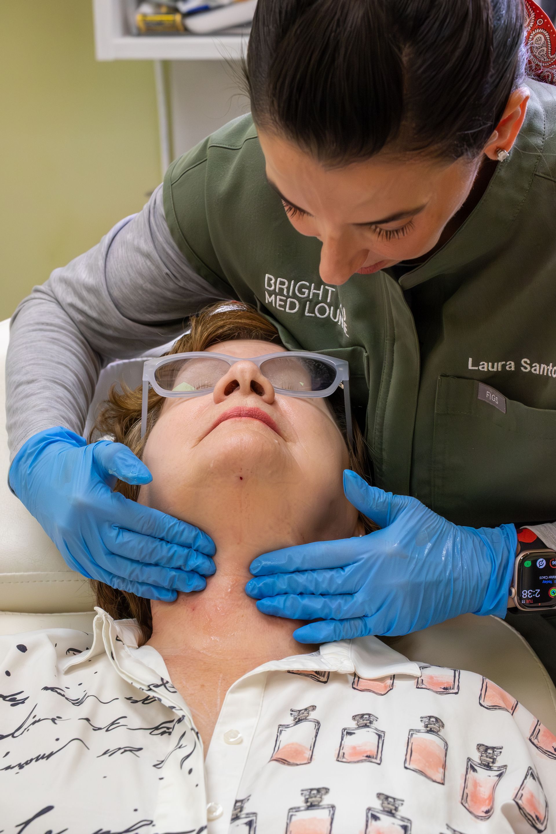 Clinician gently examines a patient’s neck while they lie back wearing glasses and a patterned shirt.