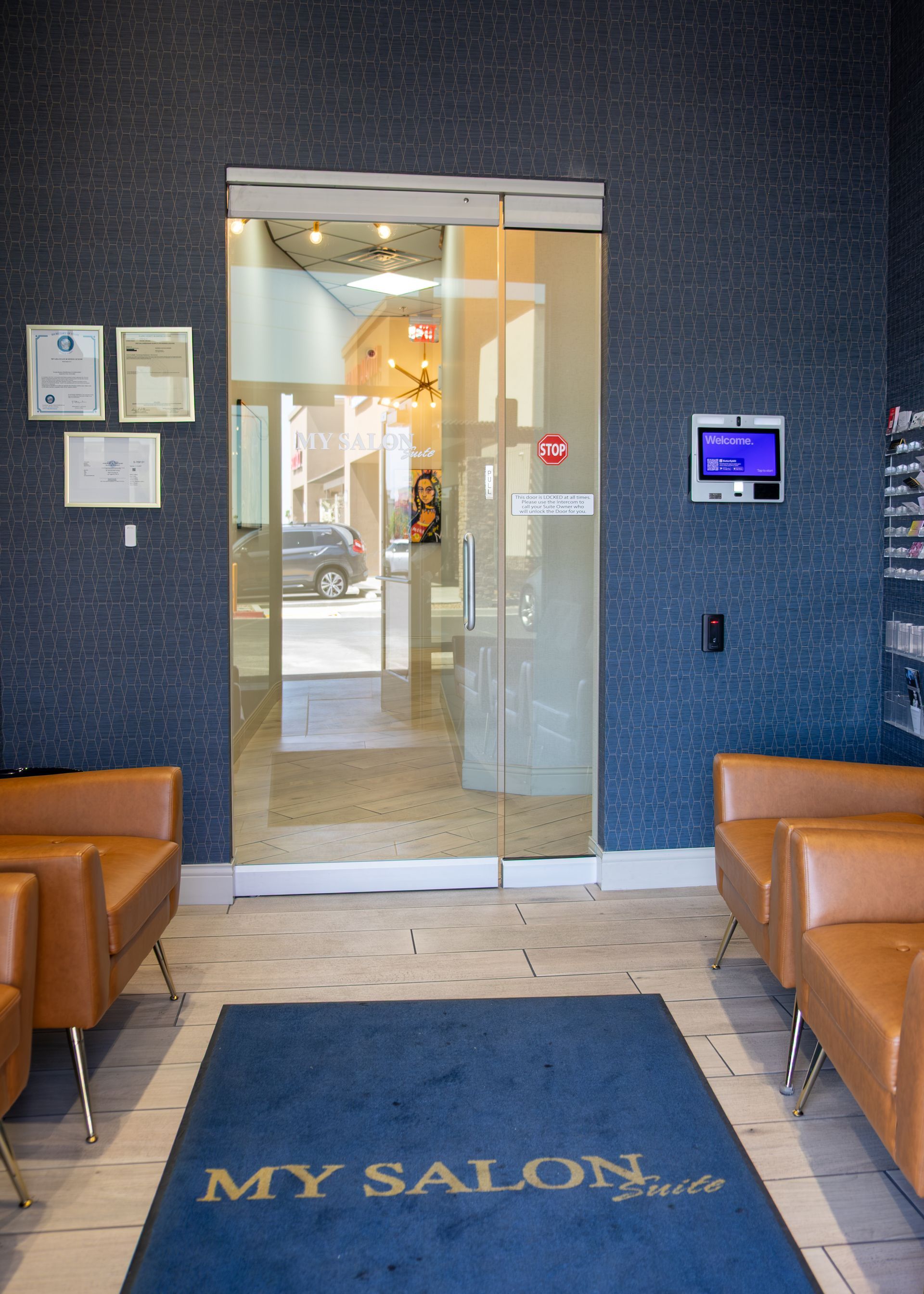 Salon entrance with glass doors, blue walls, tan chairs, and a “MY SALON” floor mat.