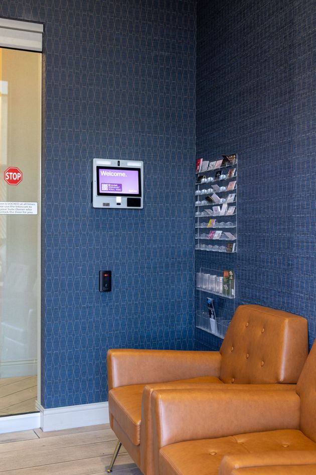 Lobby corner with an orange chair, brochure rack, wall-mounted screen, and glass door.