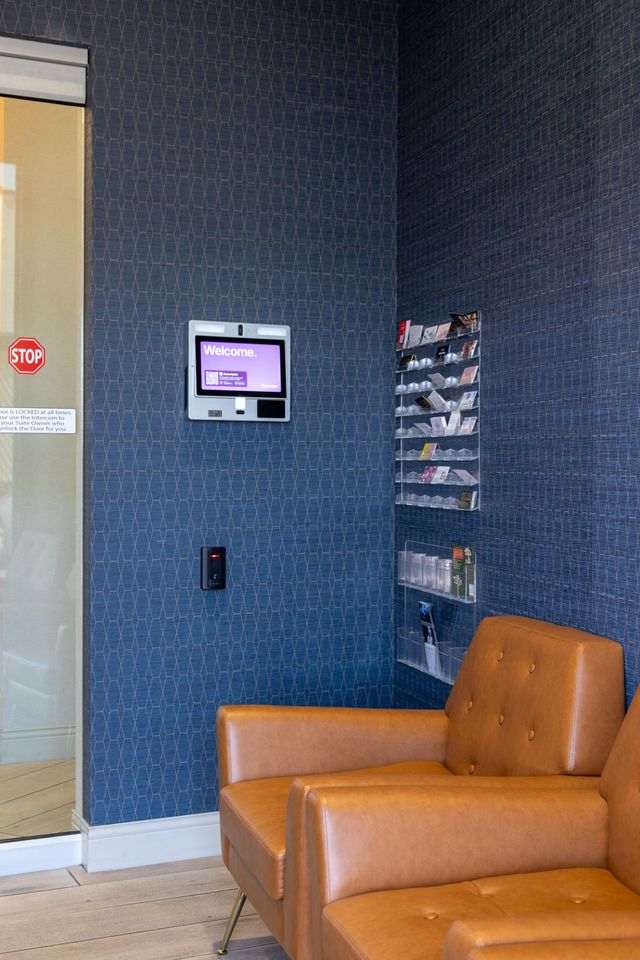 Lobby corner with an orange chair, brochure rack, wall-mounted screen, and glass door.